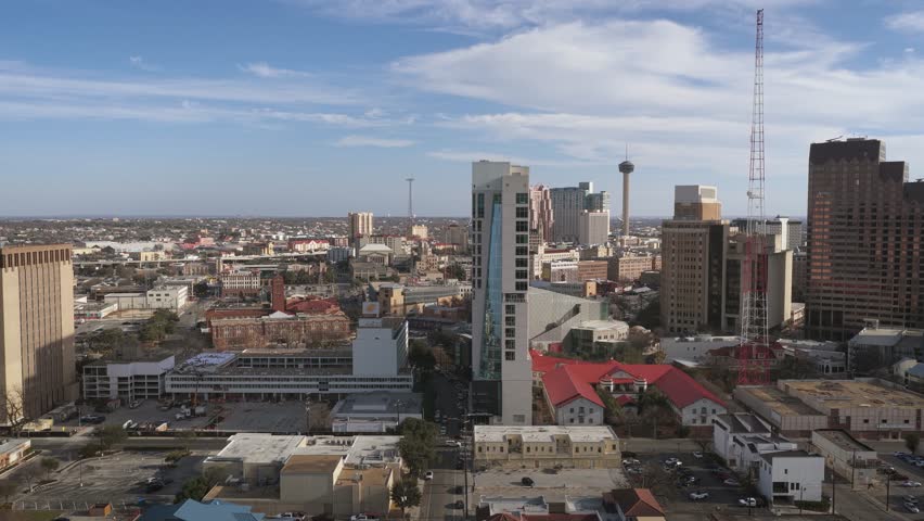 Aerial drone shot of downtown San Antonio with many buildings on a slightly cloudy day. Showing bustling city life and Texas downtown setting.