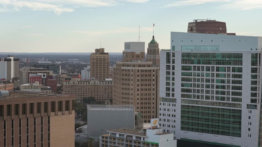 Aerial drone shot of downtown San Antonio with many buildings on a slightly cloudy day. Showing bustling city life and Texas downtown setting.