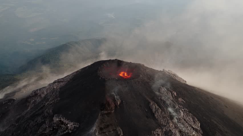 Slow orbit aerial of Fuego Volcano crater with glowing lava and steam drifting over the surrounding Guatemalan terrain.