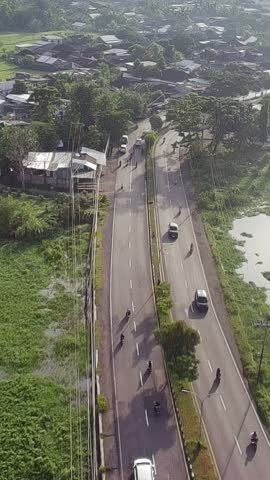 Aerial view of a rural road with vehicles and people in Indonesia. Daily life activity on the street surrounded by green landscape and houses, showing transportation and local environment.