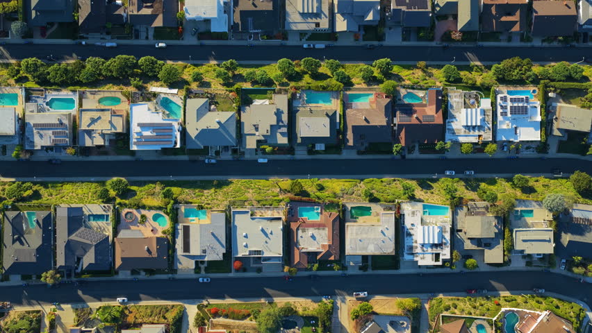 Top down drone flyover above luxury homes and modern villas in Hollywood Hills with private pools, green gardens and palm trees in bright California sunlight.