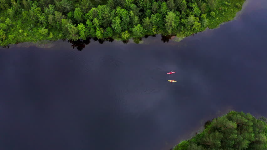 Top aerial 4K footage of yellow and red kayaks with two persons paddling kayak floating by mountain lake surrounded pine trees forest in Norway. Active people, traveling, beauty in Nature concept