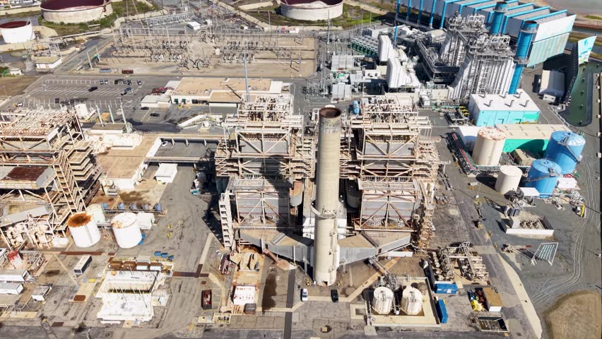 Dramatic aerial circle around the rusty smokestack of an old California oil refinery on the Pacific Coast
