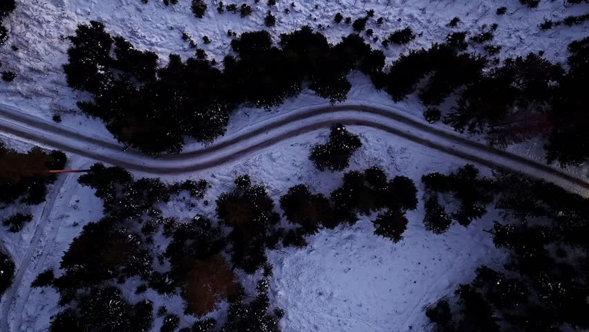 Aerial view of a logging truck driving along a snow covered forest road at night. Industrial timber transport through a dark winter woodland landscape in cold climate conditions.