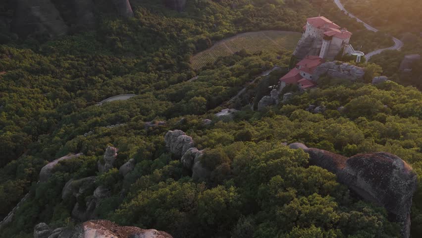 Golden sunset over Meteora rock formations and red-roofed monastery nestled among lush green forests in Greece.