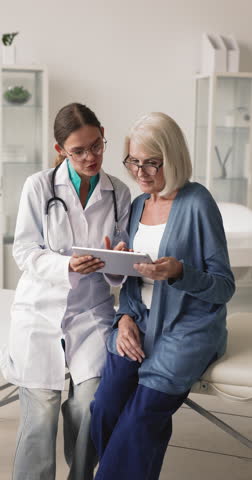 Female doctor and middle-age patient reviewing diagnostic information or test results on digital tablet, therapist explain treatment plan, medical procedure, give health advices during visit in clinic