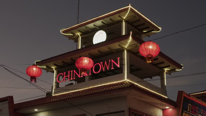Chinatown entrance tower lit with red lanterns at dusk, glowing warm lights outline tower awnings