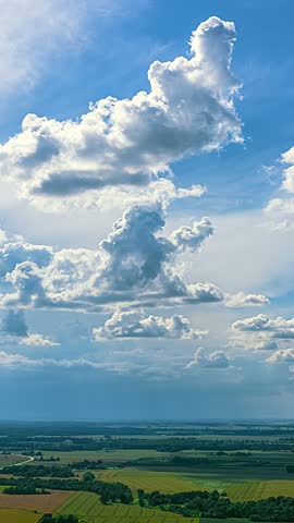 Panoramic countryside under towering clouds billowing growing and spinning with shadows mirroring on farmfields, vertical timelapse