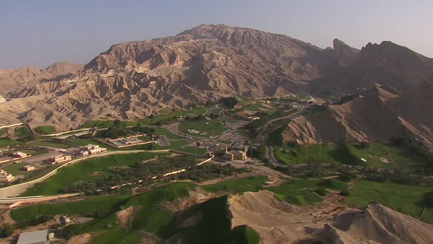 aerial view of green oase in the middle of the desert with a giant mystic mountain behind