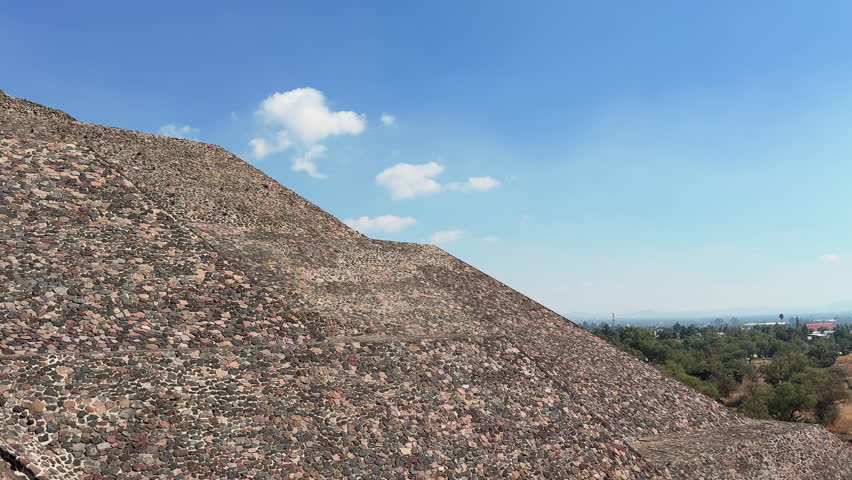 High viewpoint over Teotihuacan’s Pyramid of the Moon terraces and plaza with distant Pyramid of the Sun and hazy mountains, cinematic Mexico travel landscape b-roll.