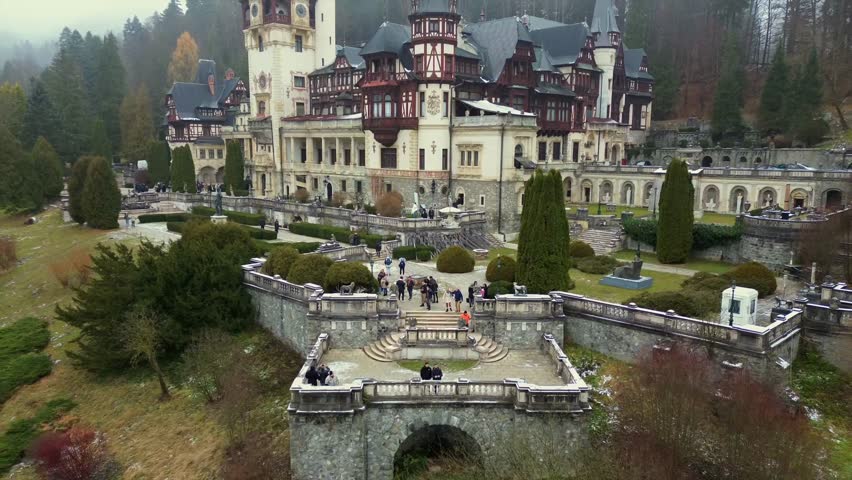 Cinematic drone pullback revealing the Neo Renaissance Peles Castle in Sinaia Romania featuring ornate architecture and misty pine forest in the Carpathian Mountains during autumn
