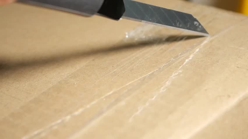 Opening a cardboard box with a utility knife in a workspace area