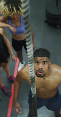 Fitness, rope climbing and man in gym for bodybuilder training, muscle strength and workout. Athlete, above and person with equipment for intense exercise, endurance and strong body with team support