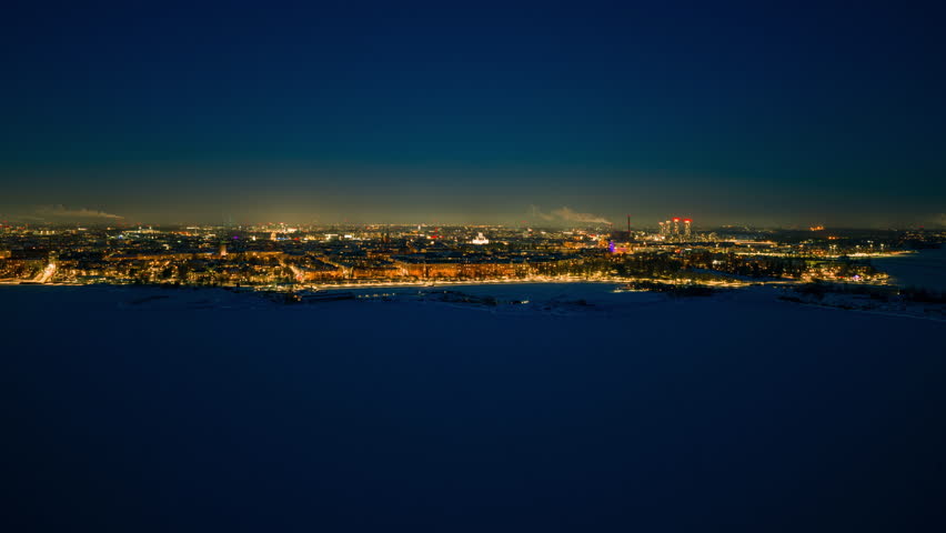Aerial hyperlapse frozen sea toward illuminated Helsinki, winter dusk in Finland