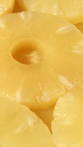 Juicy pineapple slices in syrup fill the closeup frame showing circular rings with glossy surface texture
