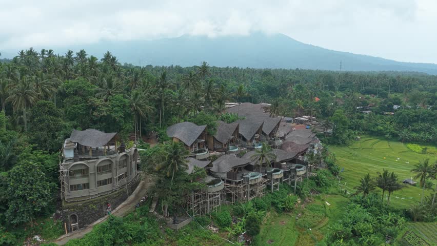 Unfinished luxury hotel complex under construction surrounded by a lush tropical jungle, rice paddies, and a distant volcano in bali