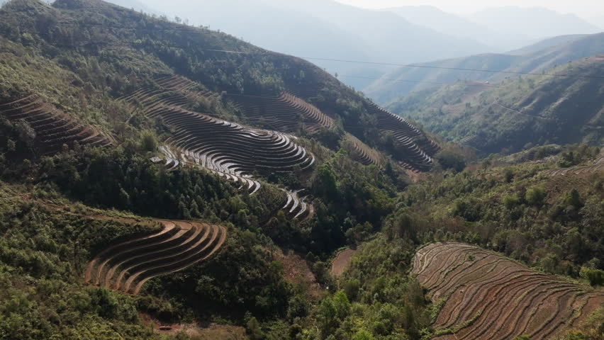 Gliding aerial footage presents a wide scenic ridge of rice terraces with layered mountains beyond at sunrise in Mui Giay, Mu Cang Chai district, Yen Bai province, Vietnam.