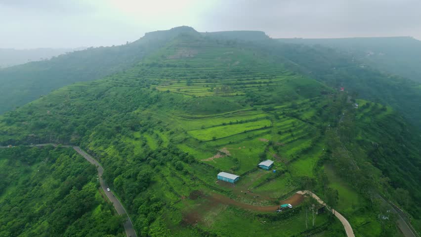 A drone glides over the lush green mountains of Panchgani, Maharashtra, as monsoon mist weaves through the valleys and treetops, creating a serene and mystical atmosphere over the Western Ghats