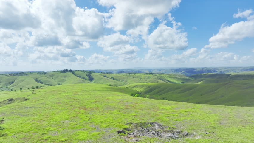 A large, grassy hillside with a clear blue sky. The sky is filled with clouds. Shot on East Sumba, Indoensia.