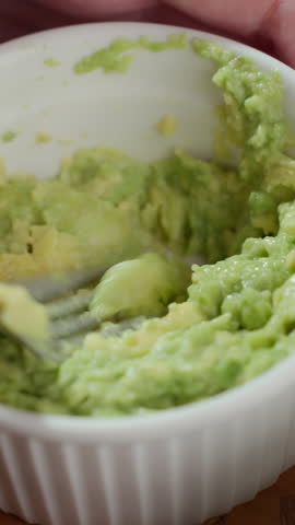 Close up of person mashing avocado flesh in bowl with fork. Concept of healthy breakfast, avocado toast preparation and vegetarian home cooking