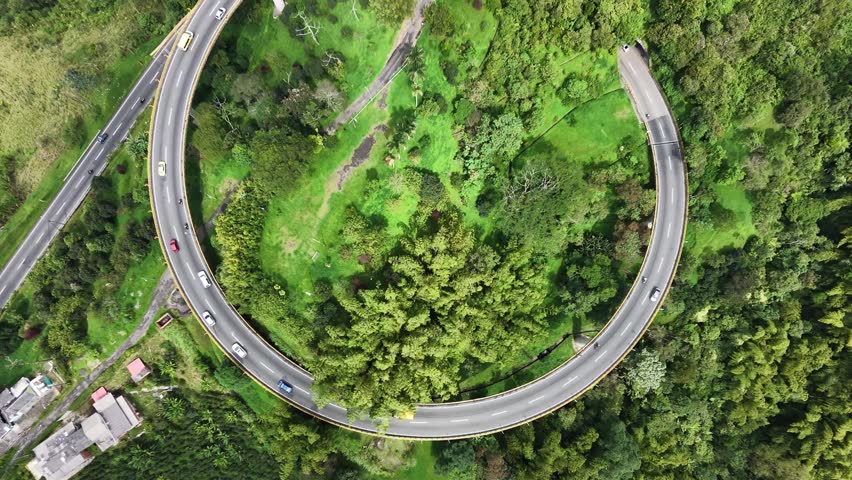 Top Down Aerial View of a Spiral Highway Bridge Surrounded by Lush Green Forest with Cars Moving Through the Canopy