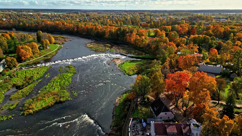 Winding river meanders through green fields and pastures, with vibrant autumn trees and rural landscape on its banks.