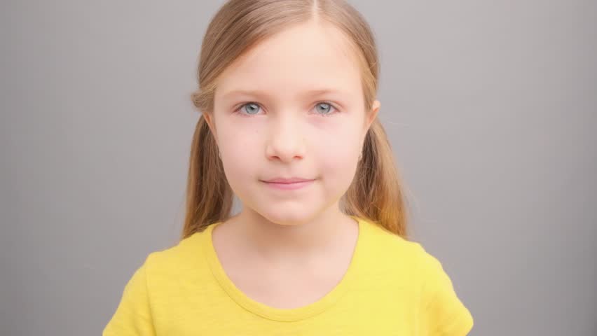 Portrait of a cute little girl with blonde hair in pigtails smiling against a grey background