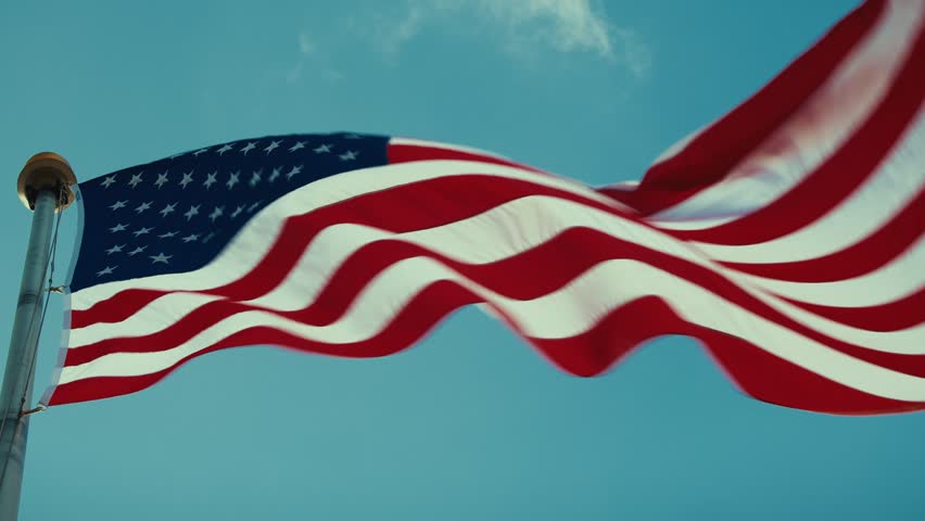 Close up American flag waving in the wind against clear blue sky, patriotic United States symbol of freedom.