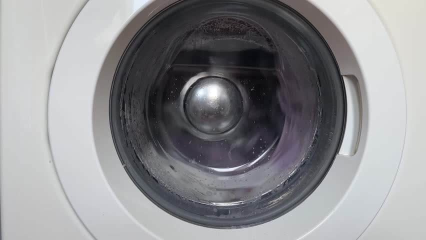 washing machine in action,drum turning behind the glass door with suds and water movement,steady laundry cycle audio and home appliance concept of cleaning clothes
