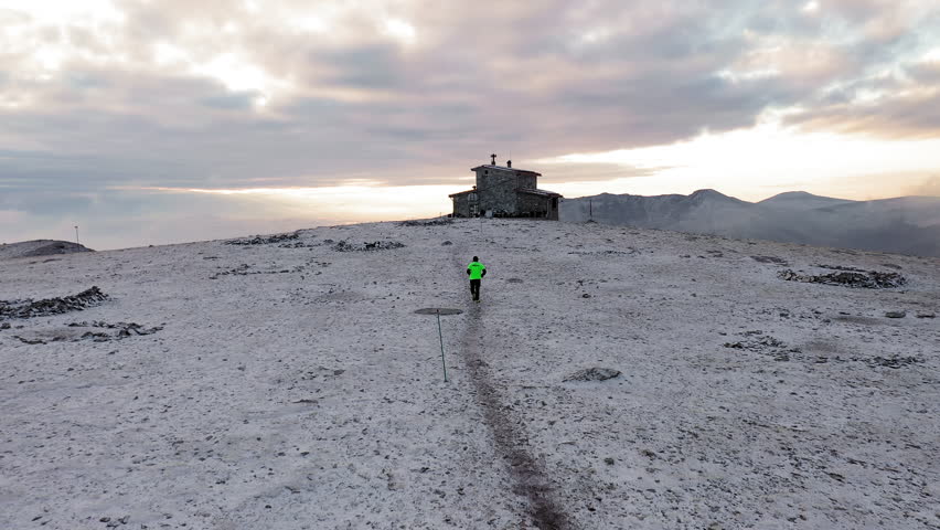 Drone shot of a lone runner on Mount Olympus running towards Christos Kakkalos refuge at sunrise moving through a snowy alpine landscape