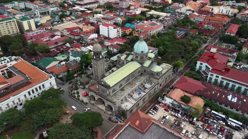 Aerial oblique view reveals Manila Cathedral with prominent dome and bell tower rising above dense Intramuros district surrounded by colonial-era buildings with terracotta rooftops and narrow streets