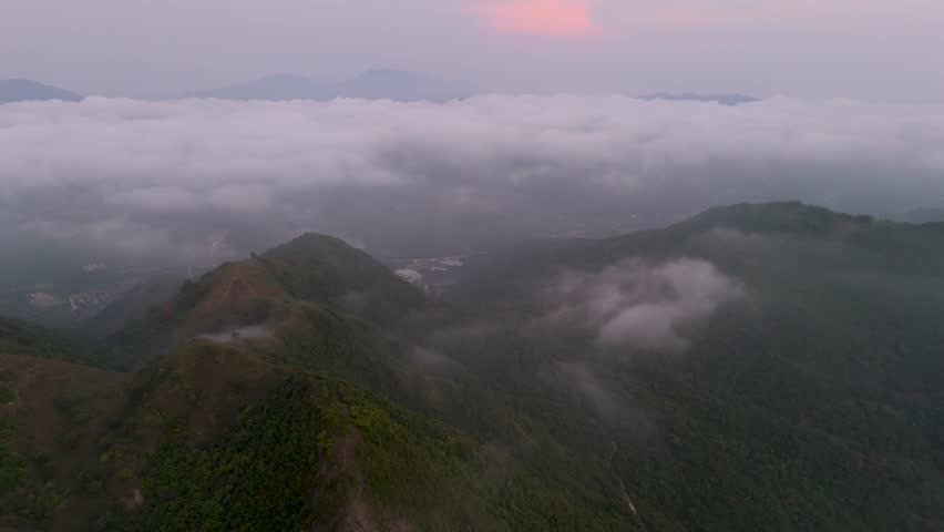 Witness a stunning aerial panorama of a town situated within a large mountain valley. Soft clouds drift across the sky and over green hills, creating a peaceful daytime setting.