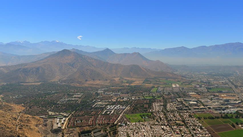 Wide aerial view of residential neighborhoods in Santiago, Chile with Andes mountains and valley landscape.
