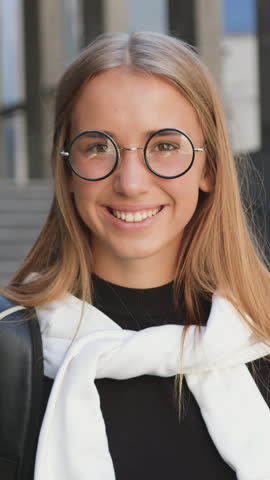 Nice cheerful lucky 25-aged light-haired stylish girl in eyeglasses looking at camera with sincerely smile,standing near modern building on sunny day,close up