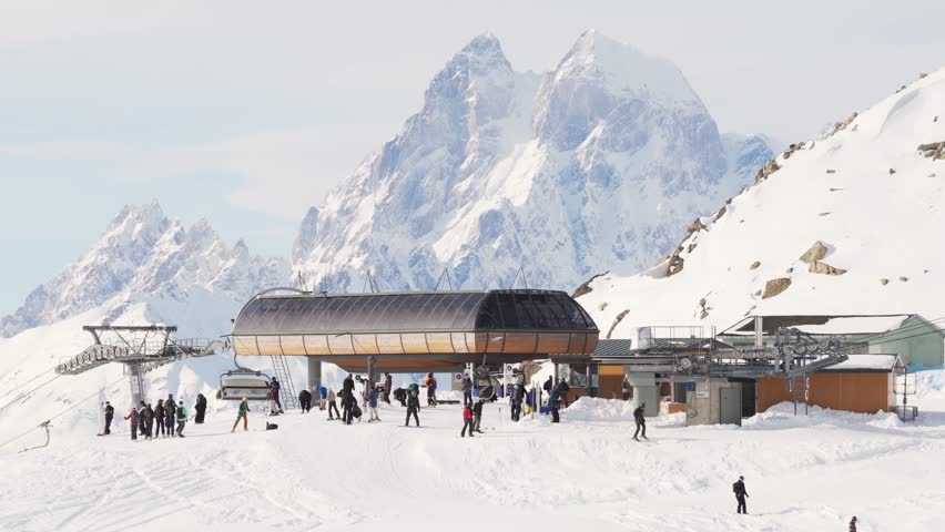 Mestia, Georgia - 25th february, 2026: Aerial panoramic view crowded Tetnuldi upper lift station with skiers and snowboarders, chairlift terminal on snowy ridge, Ushba peak towering behind