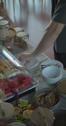 A man is reaching for a plate of fruit. The table is full of fruit and other food items 