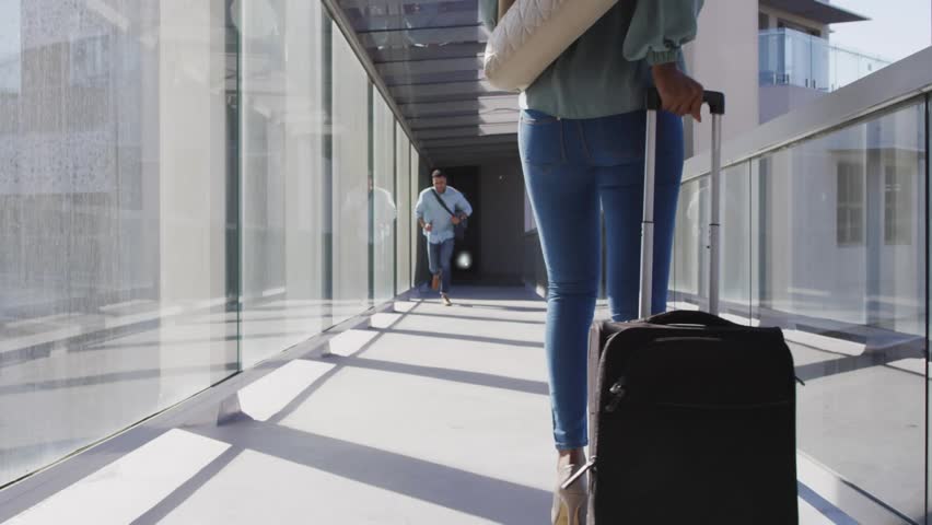 Woman pulling suitcase approaching man on bridge, blue icons expanding linking users for travel. Skywalk, glass, reflections, urban, movement, connectivity, commuter