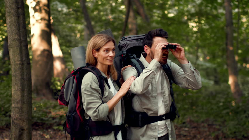 Couple Enjoying Nature While Hiking in the Woods Using Binoculars During a Sunny Day