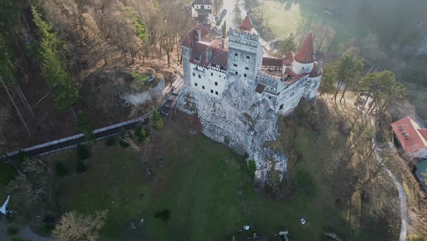 Cinematic high angle drone shot of the legendary Bran Castle in Transylvania Romania known as Draculas Castle featuring medieval fortress walls on a steep cliff with autumn forest background