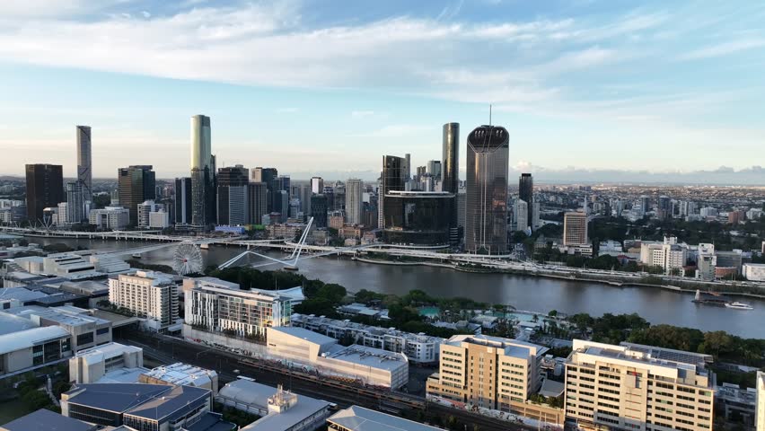 Slow drone side tracking at golden hour along the Brisbane River, passing South Bank toward Queens Wharf and The Star Brisbane towers with the CBD skyline, Brisbane, QLD, Australia