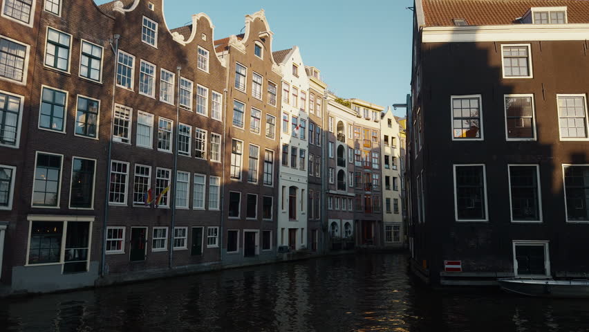 Iconic gabled canal houses along the Groenburgwal canal in Amsterdam illuminated by warm sunlight and reflecting in the water