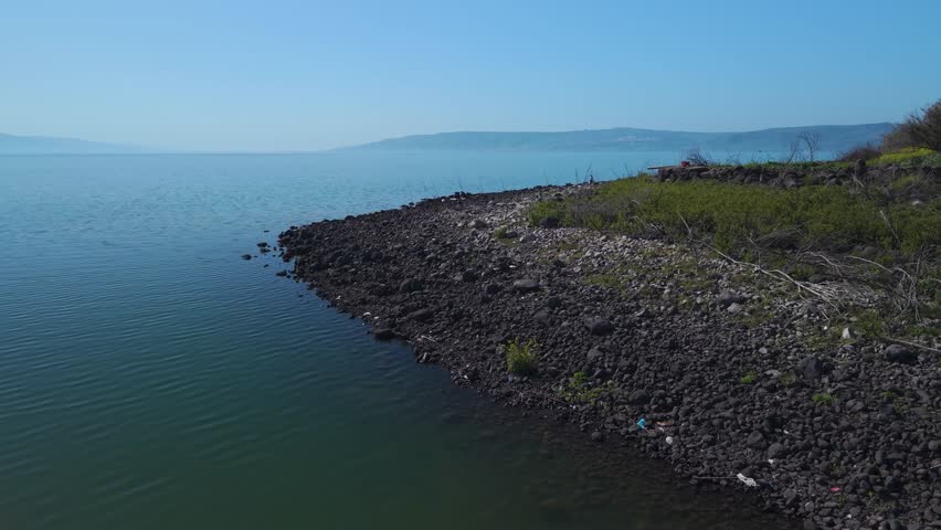 Lake Kinneret in Israel with a drone shot over the rocky Amnon Beach coast and the Golan Heights mountains behind.
