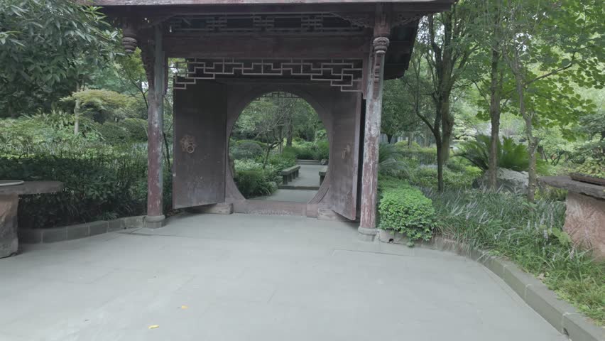 Traditional Chinese moon gate opening to garden path with trees and greenery, medium establishing push in to park