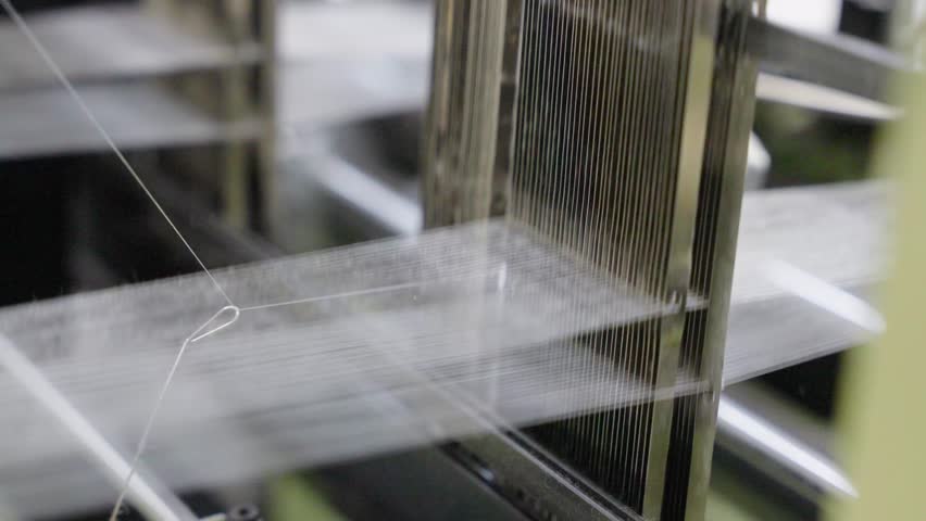 Close-up of a loom machine in action, showcasing threads, moving parts, and the weaving process, ideal for textile manufacturing, craftsmanship, industrial production, and machinery visuals.