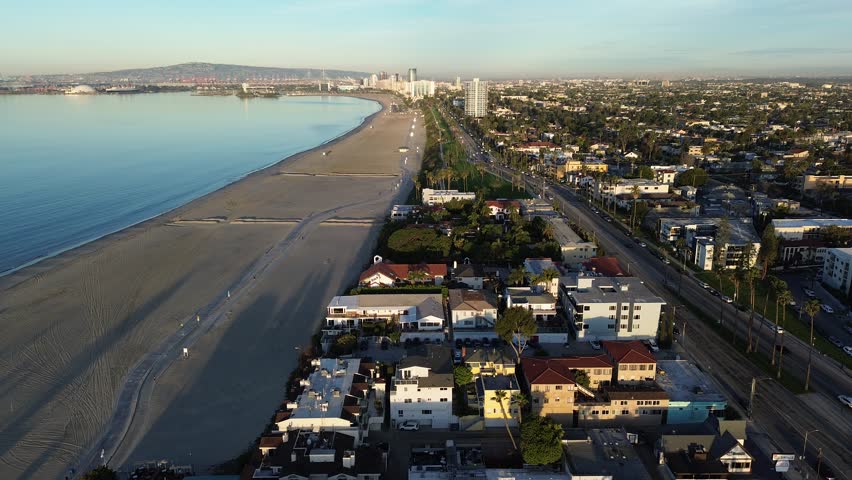 Coastal grid overview from Belmont Shore dense blocks frame East Ocean Blvd near Veterans Memorial Pier. Warm light over mixed roofing, soft beach textures, long palm shadows, Long Beach, CA. USA