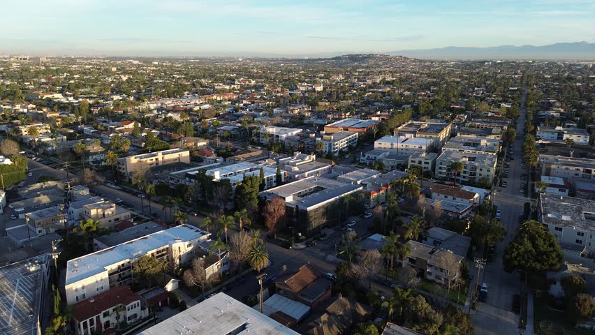 Alamitos Bay Peninsula south of East Ocean Blvd leads toward Belmont Shore beachfront blocks. Subtle roof gradients, palm-lined streets, marine haze, dense residential grid in Long Beach, CA. USA
