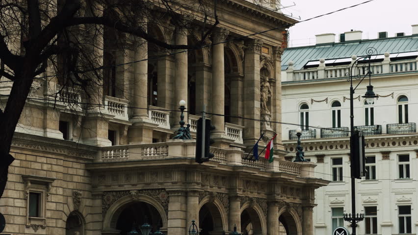 Exterior view of historic opera house building in Budapest, Hungary. Ornate European architecture with columns, statues and national flags in urban setting.