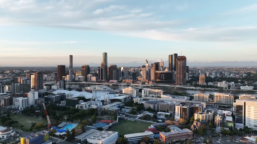 Slow drone side tracking at golden hour, keeping Musgrave Park in the foreground while the Brisbane CBD skyline and Queens Wharf towers stretch across the horizon, Brisbane, QLD, Australia