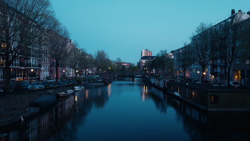 Amsterdam canal during the blue hour, with illuminated buildings, houseboats and reflections on the deep blue water
