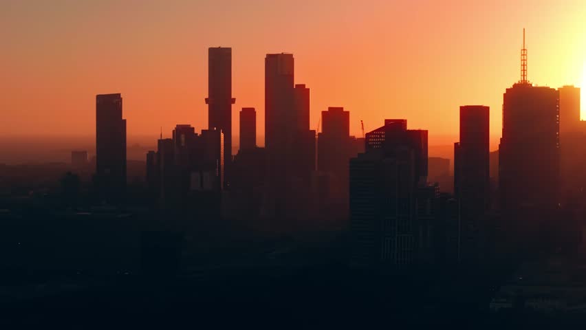 Aerial sunset over Melbourne skyline from Abbotsford with city silhouetted in orange glow, establishing urban abstract Australian metropolitan, tracking right